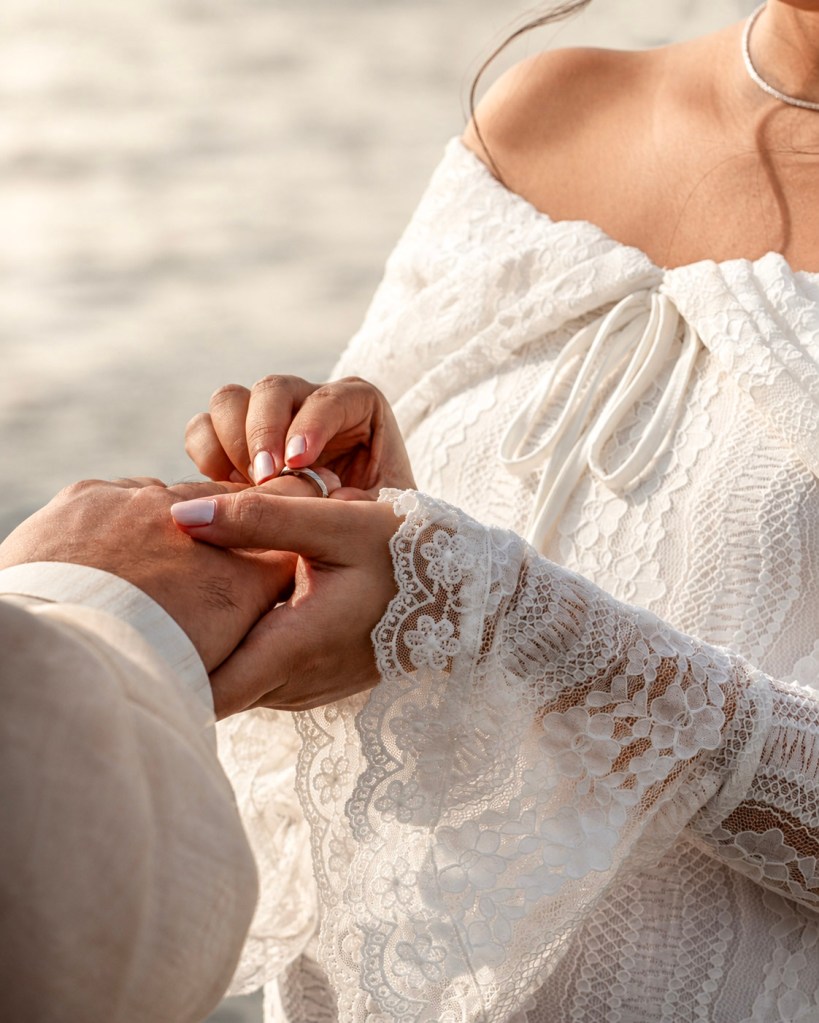 Close-up of a bride placing a wedding ring on her partner’s finger during an intimate wedding ceremony by the water in Sweden.